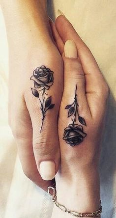 two people holding hands with matching tattoos on their fingers, one has a rose and the other has a leaf