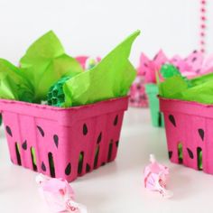 two watermelon shaped baskets filled with green leaves and pink tissue pom poms