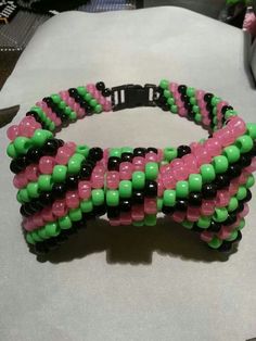 a pink and green beaded bracelet sitting on top of a white table next to a computer keyboard