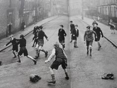 a group of young boys playing soccer on a street in the early 1900's