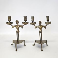 two bronze candlesticks with people holding them in the shape of stars and an upside down candle holder