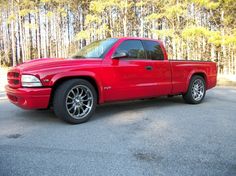 a red pick up truck parked in a parking lot next to some trees and bushes