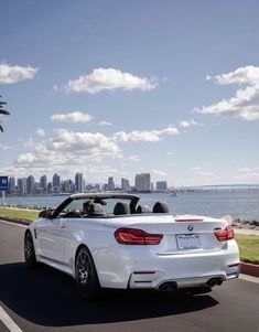 a white convertible car driving down the road next to water and cityscape in the background