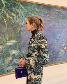 a woman standing in front of a painting holding a blue purse and looking at it