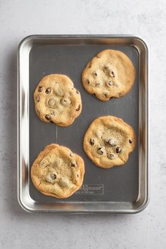 four chocolate chip cookies sitting on top of a cookie sheet in a baking pan, ready to be baked