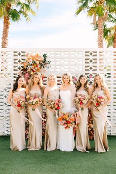 a group of women standing next to each other holding bouquets in front of a white fence