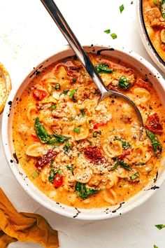 two bowls filled with pasta and spinach on top of a white table next to bread