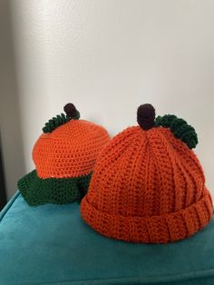 two knitted pumpkin hats sitting on top of a blue pillow