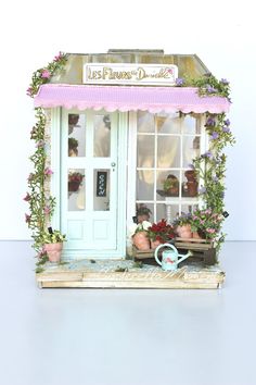 a doll house with flowers and potted plants in front of the door that is open