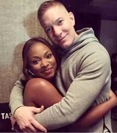 a man and woman hugging each other in front of a wall