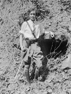 an old black and white photo of a young boy in the woods with a cow