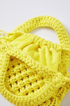 a crocheted yellow purse with a knot at the top and bottom, sitting on a white surface