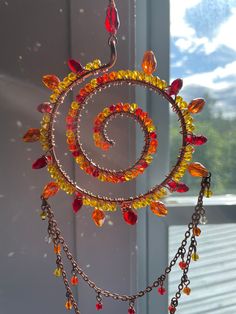 a spiral wind chime with beads and chains hanging from it's center, in front of a window