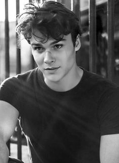 black and white photograph of a young man in front of a fence with his hands on his hips