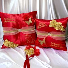 two red pillows with gold flowers and ribbons on top of a white sheeted bed