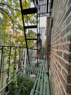 a woman standing on the top of a metal stair case next to a brick wall