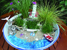 a bowl filled with plants and rocks on top of a wooden table next to grass