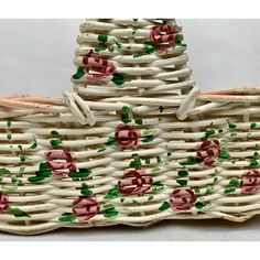 a basket with roses painted on it sitting on top of a white cloth covered table