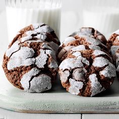 chocolate crinkle cookies with powdered sugar are on a plate next to two glasses of milk