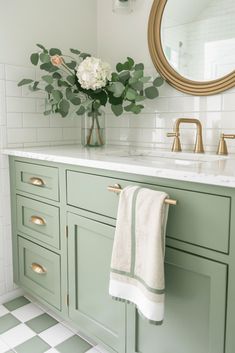 a bathroom with green cabinetry and white tile flooring, flowers in a vase on the sink