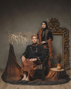 two people sitting on a chair in front of a mirror with an ornate frame behind them