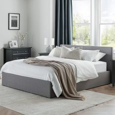 a bed with white sheets and pillows in a bedroom next to a large window on top of a wooden floor