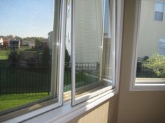 an open window with blinds on the outside and grass in the back yard behind it