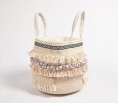 a small white basket with fringes and beads on the handles, sitting against a white background