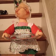 a doll sitting on top of a set of stairs wearing an apron and holding a tray