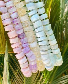 several beads hanging from a palm tree in the sun with leaves around them and one bead is pink, white and purple