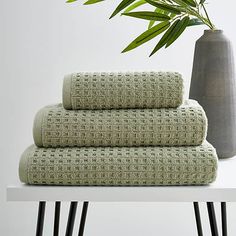 a stack of towels sitting on top of a table next to a vase with a plant in it