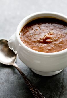 a white bowl filled with soup next to two spoons