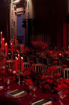 a long table is set with red flowers and candles for an elegant dinner or party