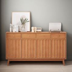 a sideboard with books and pictures on it next to a plant in a vase