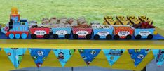 a table topped with a train cake and lots of desserts on top of it