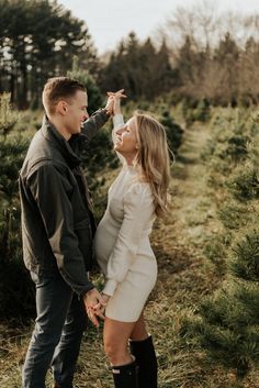 a man and woman standing next to each other in front of christmas tree farm trees