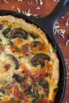 an omelet with mushrooms and cheese in a pan on a wooden table next to utensils