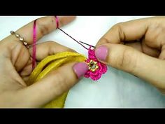 two hands are working on a piece of fabric with pink and gold beads, while another hand is holding a yellow ribbon