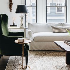 a living room with white couches and green chairs in front of two large windows