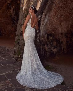 a woman standing in front of a stone wall wearing a wedding dress with an open back