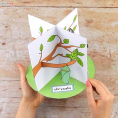 someone holding up an origami card with a tree in the middle and leaves on it