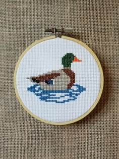 a cross stitch duck sitting on top of a body of water in front of a brown background