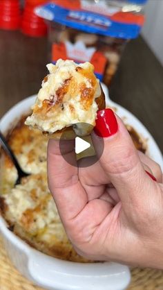 a hand holding a piece of food in front of a bowl of macaroni and cheese