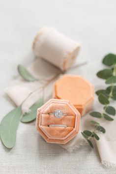 two wedding rings sitting on top of an orange ring box next to eucalyptus leaves and white linen