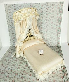 a dollhouse bed made out of fabric and lace with a clock on the top