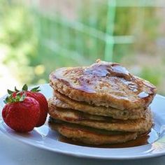 a stack of pancakes sitting on top of a white plate next to a red strawberry