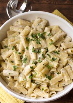 a bowl filled with pasta and parsley on top of a yellow napkin next to a fork