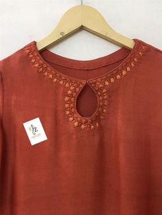 an orange top with embroidered details hanging on a wooden hanger next to a white wall