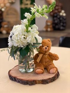 a teddy bear sitting next to a vase filled with white flowers on top of a wooden slice