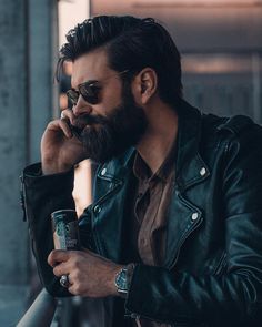 a man with a beard and glasses is talking on the phone while holding a beer